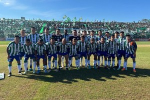 El plantel y su gente. La totalidad de los jugadores que componen la plantilla de San Miguel (con su hinchada detrás), que este martes logró el ascenso a la Primera Nacional en la cancha de Platense al vencer a Douglas Haig a través de los penales.